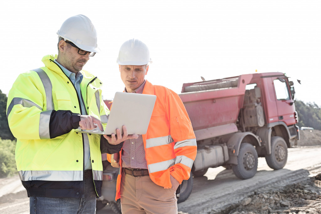 Two men in vests and hard hats using a laptop on a construction site